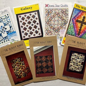 May include: A collection of eight quilt patterns featuring various designs, including stars, hearts, and geometric shapes. The patterns are printed on brown paper with the title "The Buggy Barn" and the name of each pattern.