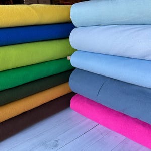 May include: A stack of colorful fabric swatches in various shades of blue, green, yellow, brown, and pink. The fabric is folded neatly and arranged in a vertical stack.