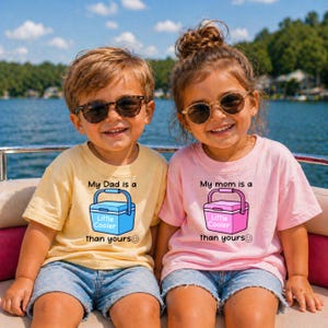 Może przedstawiać: Dwoje dzieci w okularach przeciwsłonecznych i koszulkach z napisem "My Dad is a Little Cooler than yours" i "My mom is a Little Cooler than yours". Koszulki są żółte i różowe, z grafiką chłodziarki.