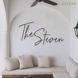 May include: A white wall with the text "The Steven" written in black cursive script. A white couch with three pillows is in the foreground.