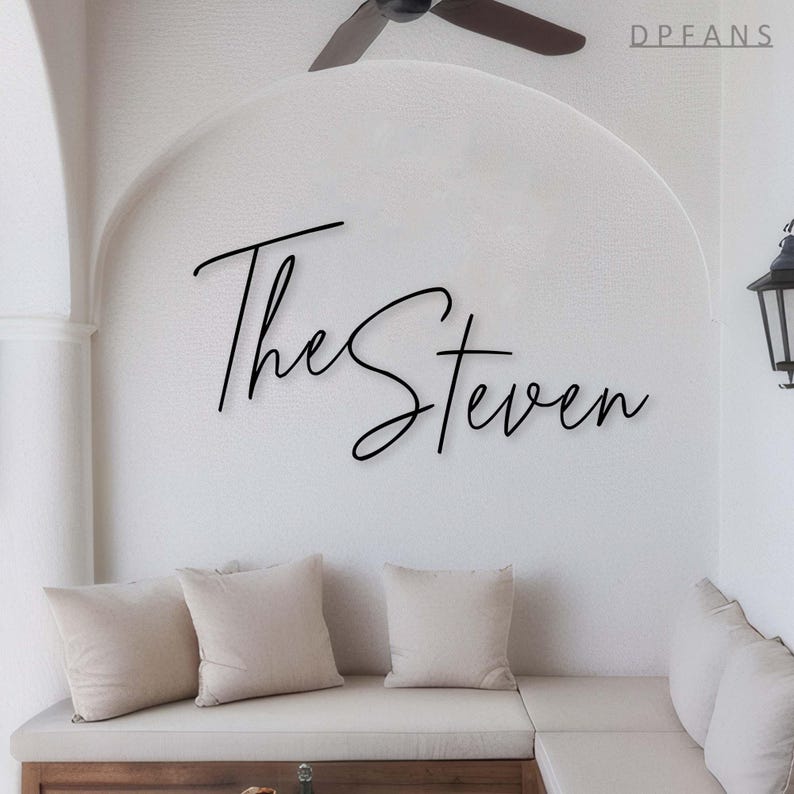 May include: A white wall with the text "The Steven" written in black cursive script. A white couch with three pillows is in the foreground.