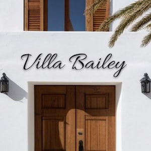 Puede incluir: Un edificio blanco con una puerta de madera y un letrero negro que dice "Villa Bailey".