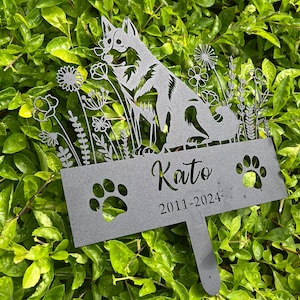May include: Black metal garden memorial with a silhouette of a dog, flowers, and the text "Kato 2011-2024".