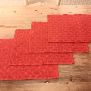 May include: Four red woven placemats of varying sizes, stacked on a wooden table.