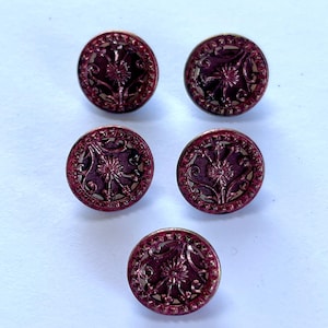 May include: Five round, antique-style buttons with a deep burgundy color and intricate floral designs. The buttons have a metallic gold-colored trim and a raised, textured pattern. Each button measures approximately 0.75 inches in diameter.
