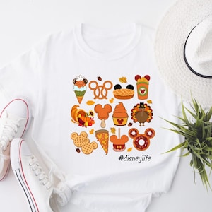 May include: White t-shirt with a graphic design of various Disney-themed food items, including Mickey Mouse ears, a turkey, a pretzel, a pizza slice, and a donut. The text "#disneylife" is printed below the graphic.