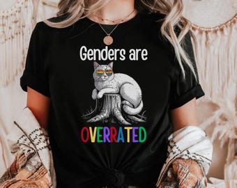 May include: Black t-shirt with the text "Genders are OVERRATED" and a graphic of a white cat wearing rainbow sunglasses. The cat is sitting on a tree stump. The shirt has short sleeves.