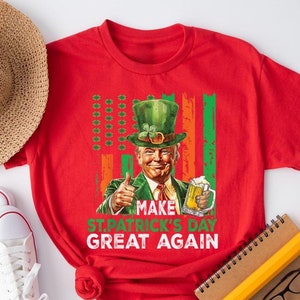 Puede incluir: Camiseta roja con un gráfico de un hombre con un sombrero de duende verde y sosteniendo una cerveza. El texto en la camiseta dice "Make St. Patrick's Day Great Again."