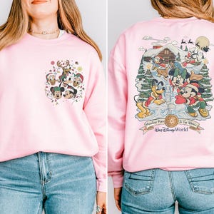 May include: Pink sweatshirt with a Christmas-themed design featuring Mickey Mouse and friends. The front of the sweatshirt has a smaller design with Mickey Mouse and friends. The back of the sweatshirt has a larger design with Mickey Mouse and friends in a winter wonderland scene. The sweatshirt has the text "Wondrous Place To See The Magic" and "Walt Disney World" on the back.