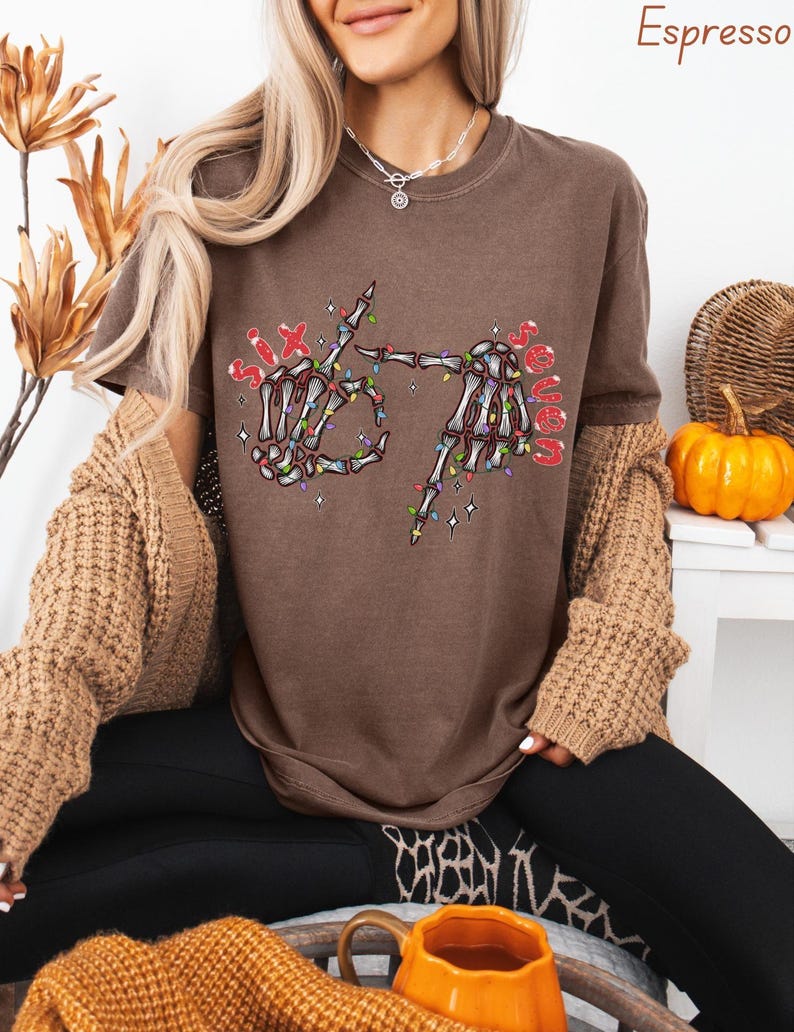 May include: Espresso-colored t-shirt featuring a skeleton hand graphic with the text "Six Senses" in red. The skeleton hands are decorated with colorful Christmas lights. The shirt is a casual, comfortable style.