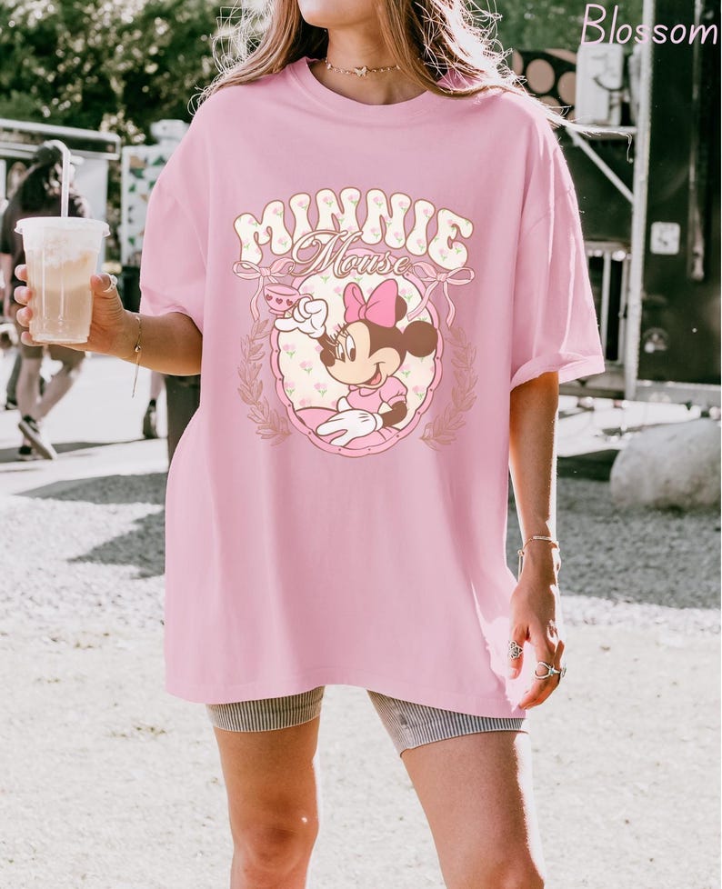 Puede incluir: Una camiseta rosa claro de gran tama&ntilde;o con un dise&ntilde;o de Minnie Mouse. El dise&ntilde;o incluye las palabras "Minnie Mouse" en una fuente caprichosa, junto con una ilustraci&oacute;n de Minnie Mouse con un vestido y lazo rosa. La camiseta es de estilo casual.