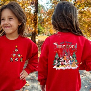 Pode incluir: Camisola vermelha de Natal com um design de Mickey Mouse e seus amigos. A frente da camisola apresenta uma &aacute;rvore de Natal com ornamentos de Mickey Mouse e seus amigos. As costas da camisola apresentam uma cena de Mickey Mouse e seus amigos em frente ao Castelo da Cinderela com o texto "Walt Disney's Disneyworld 1971".