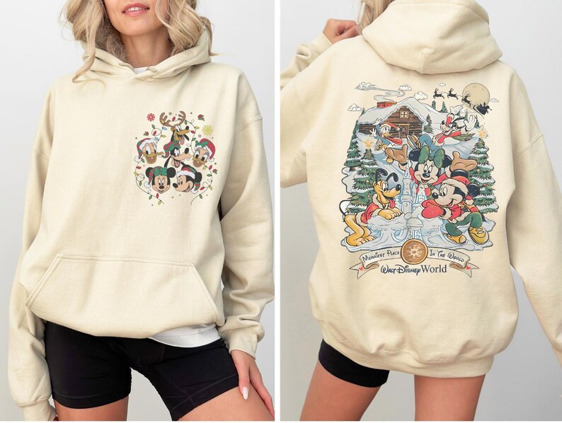 May include: A cream-colored hoodie with a Christmas-themed Mickey Mouse print on the front and a larger print on the back featuring Mickey Mouse and friends at a winter wonderland scene. The back print includes the text "Monster's Inc. In The Works Walt Disney World".