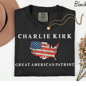 May include: Black t-shirt with the text "CHARLIE KIRK" above a graphic of the United States flag in the shape of the country. The text "GREAT AMERICAN PATRIOT" is below the flag. A gold star necklace is on the shirt.