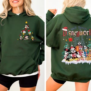 Pode incluir: Camisola de capuz verde com um design de &aacute;rvore de Natal com personagens da Disney na frente e um design "Walt Disney's Disneyworld 1971" com personagens da Disney nas costas.