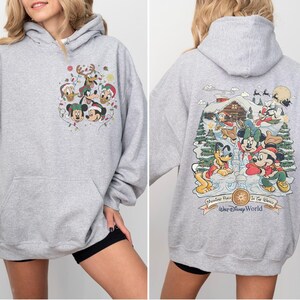 May include: Gray hooded sweatshirt with a Christmas-themed Mickey Mouse and friends print on the front and a winter scene with Mickey Mouse and friends on the back. The back print includes the text "Memories Made In The Magic" and "Walt Disney World".