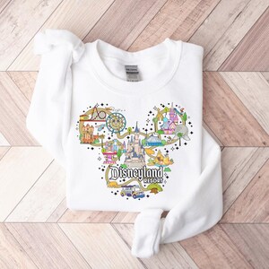 May include: White crew neck sweatshirt with a colourful Disneyland Resort graphic in the shape of Mickey Mouse's head. The design includes various park attractions and the words "Disneyland Resort".