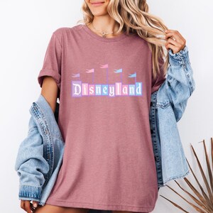 May include: A pink t-shirt with a graphic of the Disneyland castle and the text "Disneyland" in pastel colors.