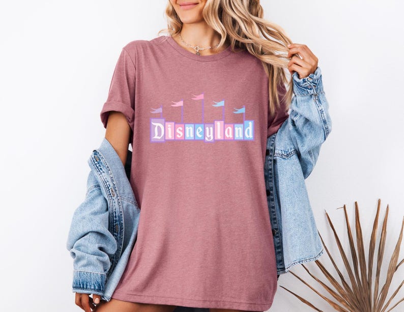May include: A pink t-shirt with a graphic of the Disneyland castle and the text "Disneyland" in pastel colors.