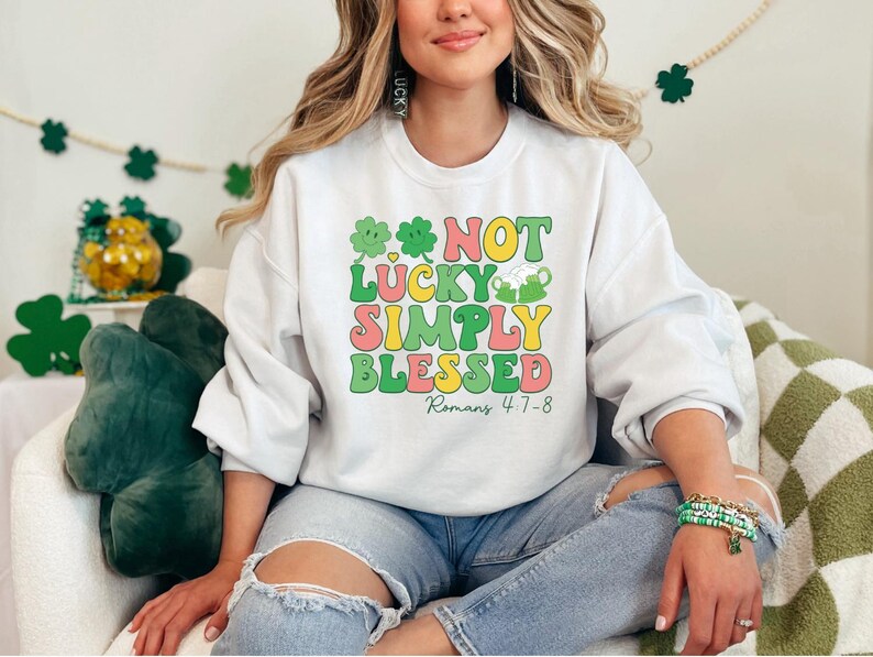 Puede incluir: Sudadera blanca con un gr&aacute;fico verde, amarillo y rosa que dice "Not Lucky Simply Blessed Romans 4:7-8".