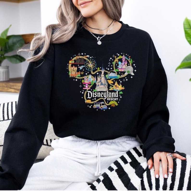 May include: Black sweatshirt with a colourful Disneyland Resort graphic in the shape of Mickey Mouse ears. The design includes illustrations of the castle, rides, and the text "Disneyland Resort". The sweatshirt is a casual style.