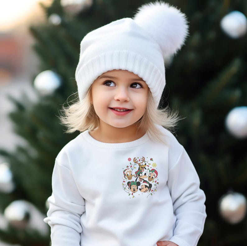 May include: A young child wearing a white sweater with a Christmas-themed Mickey Mouse print and a white knit hat with a white pom-pom.