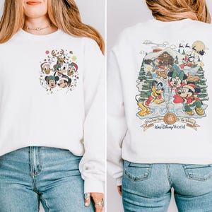 May include: White sweatshirt with a Christmas-themed Mickey Mouse design on the front and a larger design on the back. The back design features Mickey Mouse, Minnie Mouse, Pluto, and Goofy in a winter scene with a cabin and the text "Remember Place In The Magic" and "Walt Disney World".