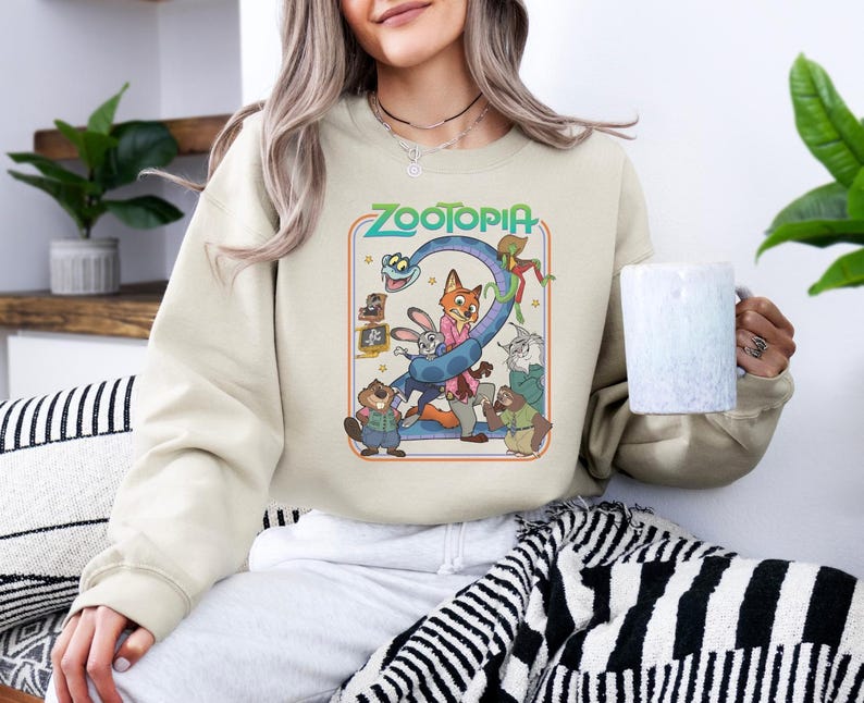 Pu&ograve; includere: Felpa color crema con una grafica colorata del film "Zootropolis". Il design include personaggi come Judy Hopps e Nick Wilde, con il titolo del film in un font retr&ograve;. La felpa &egrave; uno stile comodo e casual.