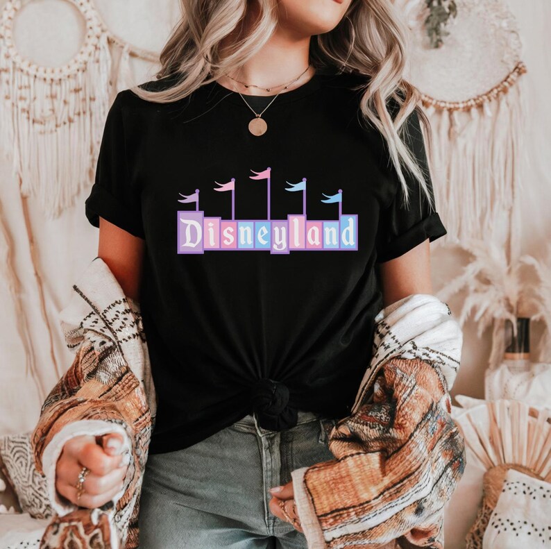 May include: Black t-shirt with a graphic of the Disneyland logo in pastel colors with flags on top.