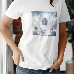 Puede incluir: Camiseta blanca con un dise&ntilde;o conmemorativo que presenta una foto de una mujer con alas de &aacute;ngel y el texto "In Loving Memory Ashley Go Feb. 20, 1988 - November 20, 2024"