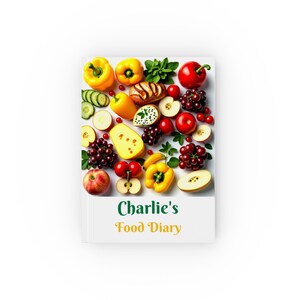 May include: A white notebook with the text "Charlie's Food Diary" on the front. The cover is decorated with a colourful collage of fruits and vegetables, including red apples, yellow peppers, green cucumbers, and red grapes.