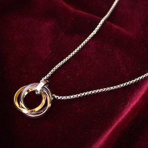 Può includere: Una collana a catena d'argento con un ciondolo a tre anelli. Gli anelli sono intrecciati e realizzati in argento, oro e argento.