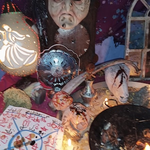 May include: A collection of mystical objects, including a carved mask, a decorative lamp, a metal bowl, and a ritualistic paper with symbols. The objects are arranged on a table with candles, creating an atmospheric scene.