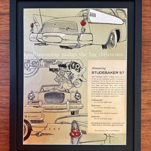May include: Framed vintage advertisement for the Studebaker '57, featuring illustrations of the car's exterior and engine. The ad is in black and white with tan and cream accents, and includes the text "Craftsmanship makes the big difference."