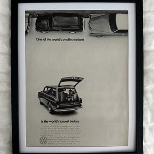 May include: A framed vintage black and white advertisement for a Volkswagen Squareback sedan. The print features a top-down view of cars and a rear view of a station wagon with an open trunk, including the text One of the world's smallest sedans is the world's largest sedan.