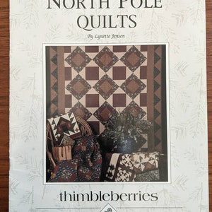 May include: A book cover titled "North Pole Quilts" by Lynette Jensen. The cover features a quilt with brown and tan diamond patterns. The "thimbleberries" logo is at the bottom.