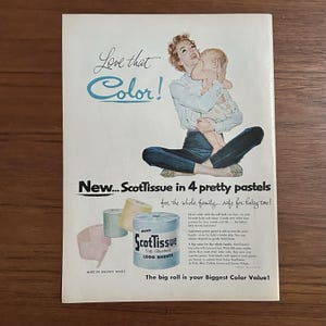 May include: Vintage advertisement for ScotTissue toilet paper. The ad features a woman holding a baby, with text that reads "Love that Color!" and "New...ScotTissue in 4 pretty pastels." The ad also shows rolls of pastel-colored toilet paper.