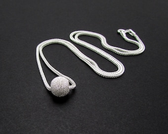 May include: A silver chain necklace with a round, sparkly, silver pendant.