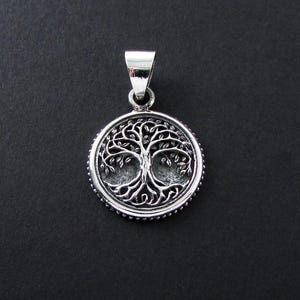 May include: A silver pendant featuring a detailed tree of life design. The pendant is round and has a beaded edge.