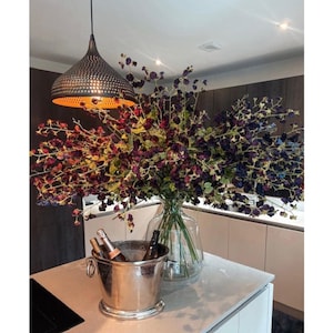 Peut inclure: Intérieur de cuisine avec un grand bouquet de fleurs violettes et vertes dans un vase en verre transparent. Un seau à glace argenté avec des bouteilles est posé sur le comptoir. Un luminaire suspendu en métal est au-dessus.
