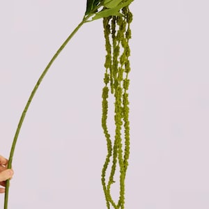 May include: A green artificial plant stem with long, cascading, textured strands. The stem has several green leaves at the top. The plant is against a white background. This decorative plant is suitable for home decor.