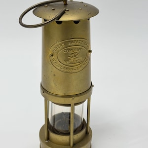 Op de afbeelding: Een messing mijnwerkersveiligheidslamp met een glazen cilinder en een handvat. De lamp heeft een label met de tekst "Miners Safety Lamp Cambrian No. 20126 W.R. Clanny - Sir H. Davy".