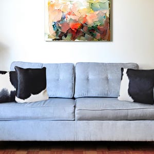 May include: A light blue sofa with three black and white cowhide throw pillows. The sofa is in a living room with a painting on the wall behind it.