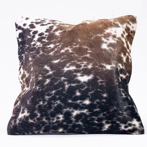May include: A square pillow with a brown, black, and white cowhide pattern.