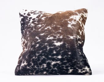 May include: A square pillow with a brown, black, and white cowhide pattern.