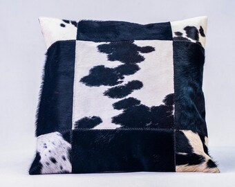 May include: Black and white cowhide patchwork pillow with a square design. The pillow is made of different pieces of cowhide sewn together to create a unique pattern.
