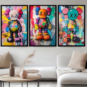 Peut inclure: Un ensemble de trois impressions d'art mural encadrées représentant des personnages de dessin animé stylisés avec des yeux en forme de X. Chaque figure est rendue avec des éclaboussures et des coulures de peinture vives et colorées.