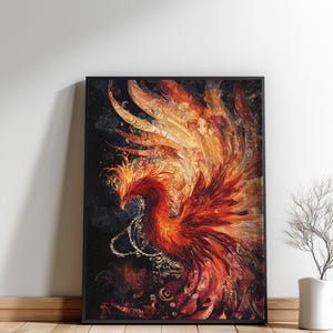 May include: Framed artwork featuring a vibrant phoenix in shades of red, orange, and gold. The mythical bird is depicted with detailed feathers and a dynamic pose against a dark background. The artwork is displayed in a black frame, leaning against a white wall.