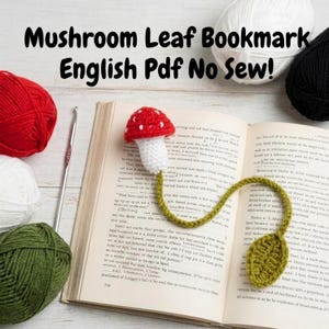 May include: A handmade crochet bookmark featuring a red mushroom with white spots and a green leaf. The bookmark is placed in an open book. The text "Mushroom Leaf Bookmark English Pdf No Sew!" is at the top.
