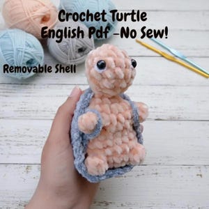 May include: A handmade crochet turtle with a removable shell. The turtle is peach-colored with a gray shell and black eyes. The image includes text that reads "Crochet Turtle English Pdf - No Sew!" and "Removable Shell."